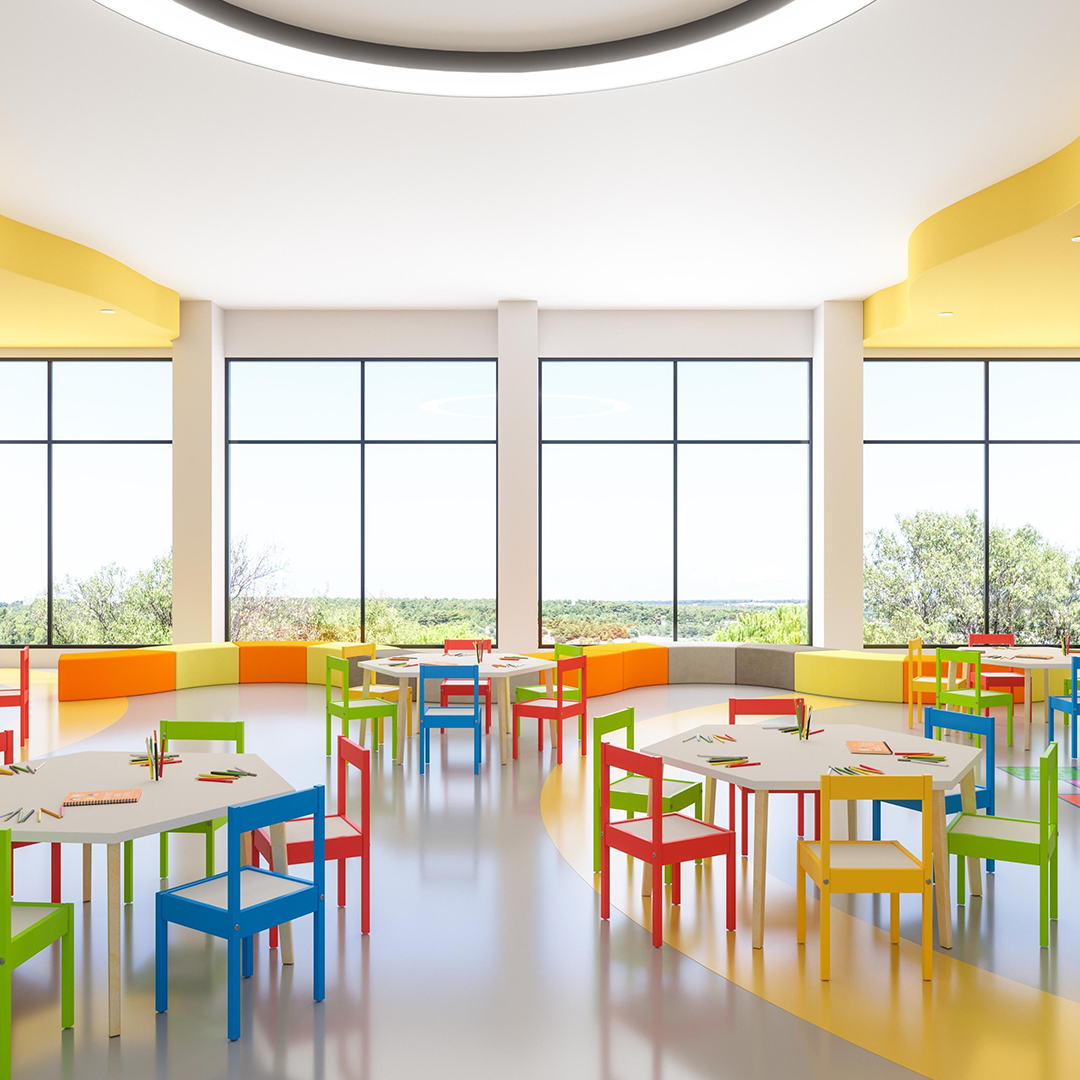 Heller Gruppenraum einer Kindertagesstätte mit Tischen, Stühlen und Spielmaterialien.
