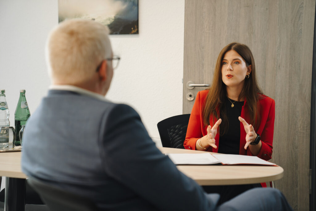 Zwei Personen führen ein Gespräch an einem Besprechungstisch in einem Büro.